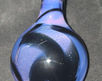 Könnte beinhalten: Ein mundgeblasener Glasflaschenverschluss mit einem Wirbeldesign. Der Verschluss weist Blautöne, Schwarz und Lila auf. Das Glas hat einen abgerundeten Boden und eine zylindrische Oberseite.