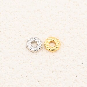 May include: Two small, circular jewelry components. One is silver-colored, the other is gold-colored. Both have a twisted rope design around the outer edge. These components are likely used in jewelry making or crafting.