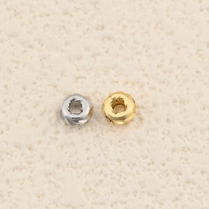 May include: Two small, round beads. One is silver-colored, the other is gold-colored. Each bead has a circular hole in the center and a textured, ridged exterior. The beads are likely used for jewelry making or other crafts.