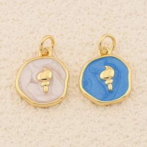 May include: Two gold-colored pendants with a torch design. One pendant has a white enamel background, the other is blue. Both pendants have a gold-colored border and a small loop for hanging.