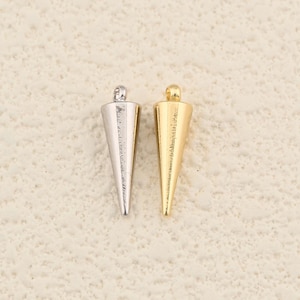 May include: Two metal cone-shaped jewelry findings. One is silver-colored, the other is gold-colored. Each has a small, rounded top. The findings are likely used for jewelry making or crafting.