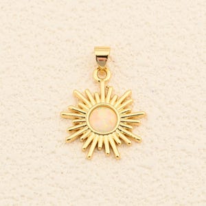 May include: Gold-colored sunburst pendant with a central, light-colored stone. The pendant has a loop at the top for a chain. The sunburst design features pointed rays extending outwards from the center, creating a radiant effect. The pendant is likely made of metal.