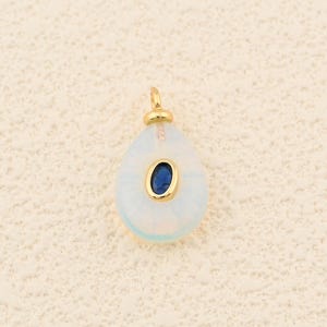 May include: A teardrop-shaped pendant with a gold bail. The pendant features a light blue, translucent body with a dark blue oval stone set in a gold bezel. The pendant is likely for a necklace or bracelet.