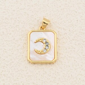 May include: Gold-tone pendant with a rectangular mother-of-pearl background. A crescent moon design, embellished with clear crystals, is centered on the pendant. The pendant has a gold bail for attaching to a chain.