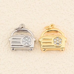 May include: Two miniature radio charms, one silver and one gold, are shown against a plain backdrop. Each charm has a vintage radio design with a circular speaker adorned with tiny, sparkling stones. The charms have a loop at the top for attaching to a chain or bracelet, ideal for jewellery making.