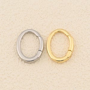 Può includere: Due chiusure ovali, una color argento e una color oro, sono mostrate su uno sfondo neutro. Le chiusure sono chiuse, mostrando le loro superfici lisce e lucide. Queste chiusure sono probabilmente utilizzate per la creazione di gioielli o come elementi decorativi.