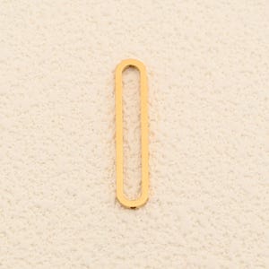 May include: A single, elongated gold-colored jewelry finding, oval in shape, is displayed against a neutral, textured background. The piece is a simple, open design, likely for use in necklaces or bracelets.
