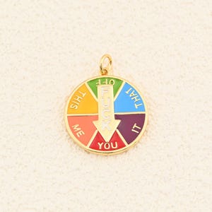 May include: A gold-colored pendant with a colorful wheel design. The wheel is divided into segments with the words "This", "Me", "You", "It", and "That". The word "F*ck" is in the center with an arrow pointing to "You".