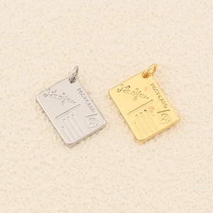 May include: Two rectangular postcard charms, one silver and one gold, with a small loop at the top for hanging. The charms have the words "Side You" and "POST CARD" engraved on them, along with vertical lines and a small stamp.