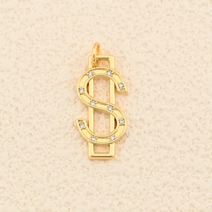 May include: A gold-colored pendant in the shape of a dollar sign. The pendant is embellished with small, clear gemstones. The design features a vertical bar with a curved "S" shape, all in a shiny gold finish.