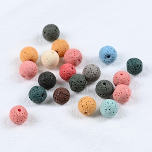 May include: A selection of multi-coloured lava rock beads, including pink, orange, blue, and grey. These round beads have a porous texture, perfect for jewellery making or craft projects. Each bead is approximately 1 cm in diameter.