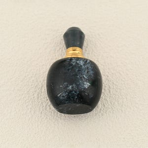 Pode incluir: Pequena garrafa escura com corpo arredondado e tampa cilíndrica escura. A garrafa tem uma faixa dourada no pescoço. A superfície da garrafa tem um padrão salpicado de branco e azul esverdeado escuro.