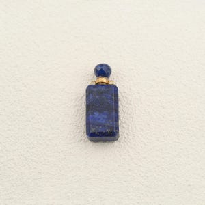 Peut inclure: Un flacon de parfum rectangulaire taillé dans une pierre de lapis-lazuli bleu profond avec des éclats de pyrite dorés visibles. Le flacon est surmonté d'un bouchon rond à facettes en lapis-lazuli et d'un col en métal doré.