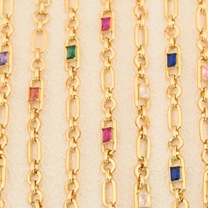 Puede incluir: Collares de cadena dorados con piedras preciosas rectangulares y coloridas. Las piedras preciosas son de varios colores, incluyendo rojo, verde, azul y rosa. Las cadenas tienen un diseño de eslabones ovalados.