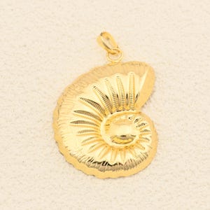 May include: A gold-colored pendant in the shape of a nautilus shell. The pendant has a detailed, textured surface with a spiral design and a loop at the top for a chain. The overall design is shiny and reflective.