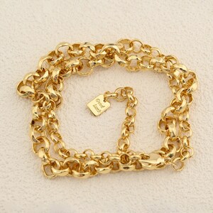 May include: A gold-colored chain necklace with large, rounded links. A small rectangular charm with the words "Good Luck" is attached. The necklace is displayed on a light-colored surface.