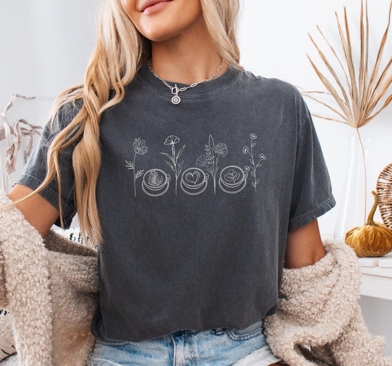 Close up of a model wearing a Pepper dark grey Comfort Colors 1717 t-shirt with a retro Coffee and Flowers graphic. Showcasing a trendy cozy barista aesthetic and soft cotton texture.