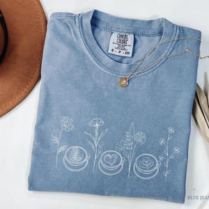 Minimalist botanical line art with coffee cups printed in cream ink on an Blue Jeans Comfort Colors t-shirt. Aesthetic coffee lover apparel.