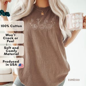 May include: Espresso-colored t-shirt with a floral and coffee cup design. The shirt features the text "100% Cotton", "Won't Crack or Peel", "Soft and Comfy Material", and "Produced in USA". The word "ESPRESSO" is also visible.