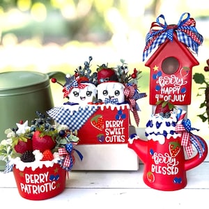 May include: A collection of red, white, and blue decorative items with berry and patriotic themes. Includes a birdhouse, teapot, and containers with text like "Berry Patriotic" and "Happy 4th of July."