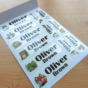 Puede incluir: Una hoja de etiquetas adhesivas rectangulares con el nombre Oliver Brown en texto negro. Cada etiqueta incluye una colorida ilustración de dibujos animados de animales, como un lobo, panda, mono, búho, tortuga, zorro, león, erizo, mapache y conejo.