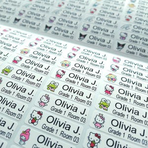 May include: A sheet of rectangular white adhesive labels featuring the printed text Olivia J. Grade 1 Room 03. Each label includes a small colourful graphic of various cartoon characters including a white cat, a green frog, and a pink rabbit.