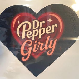 May include: A heart-shaped sticker with the words "Dr Pepper Girly" in a stylized font. The design features a red heart shape with a black background, and the text is in a cream color with a red outline.