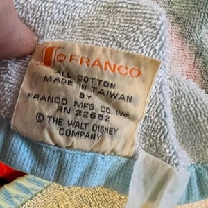 May include: Close-up of a multi-colored cotton towel with a tag that reads "FRANCO ALL COTTON MADE IN TAIWAN BY FRANCO MFG. CO. INC. RN 22662 &copy; THE WALT DISNEY COMPANY."