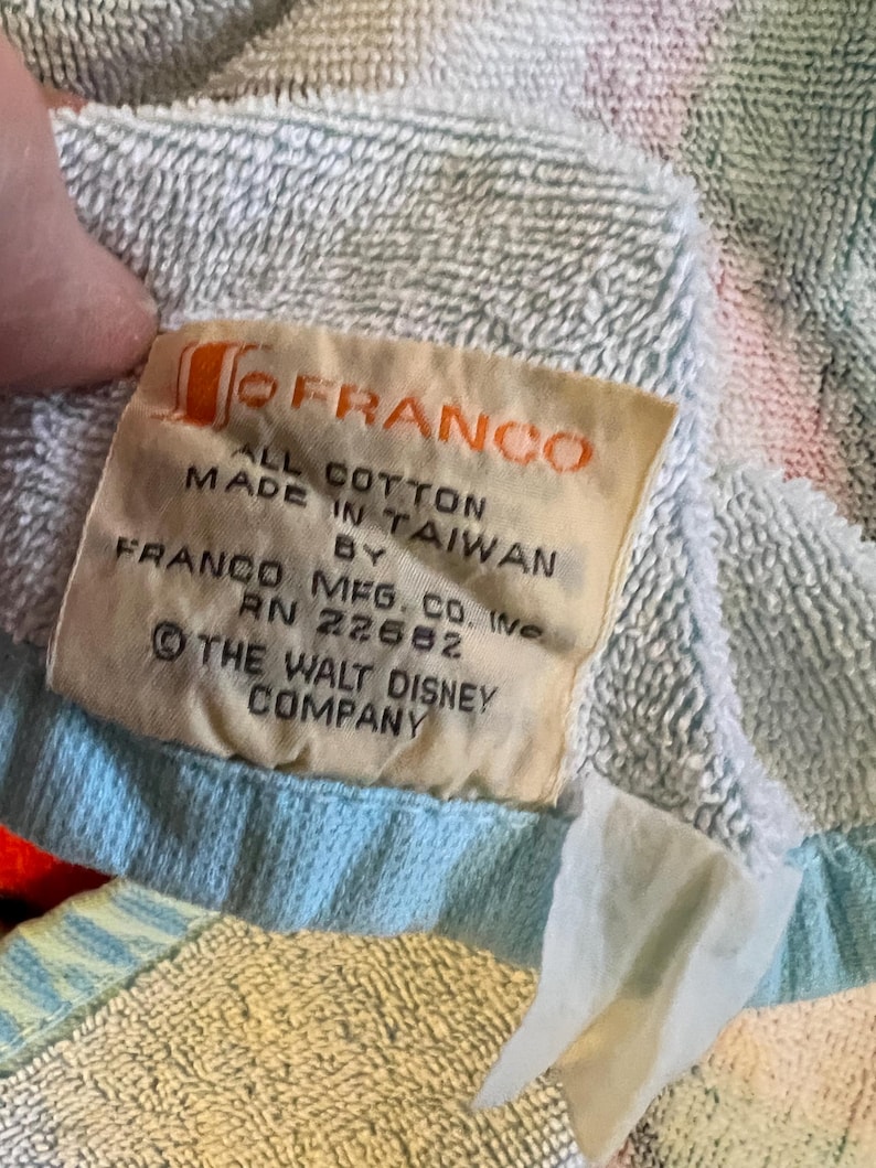 May include: Close-up of a multi-colored cotton towel with a tag that reads "FRANCO ALL COTTON MADE IN TAIWAN BY FRANCO MFG. CO. INC. RN 22662 &copy; THE WALT DISNEY COMPANY."