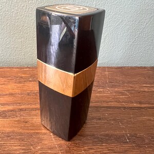 May include: A tall, rectangular black cosmetic container with a glossy finish. The object features a wide, horizontal gold-colored band encircling the middle section. The top cap displays a circular white logo with two interlocking C letters.