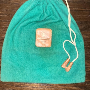May include: A green felt drawstring bag with a brown leather patch that says "Ralph Lauren" and a white drawstring.