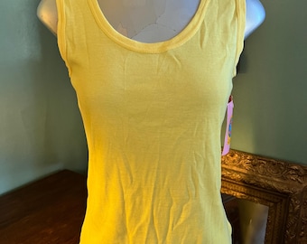 May include: A bright yellow tank top with a scoop neckline. The sleeveless top is displayed on a mannequin. The fabric has a ribbed texture. A small tag is visible on the side. The tank top is a solid color.