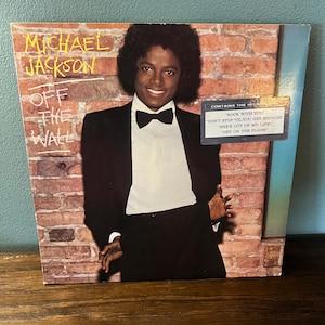 May include: Album cover for Michael Jackson's "Off the Wall." The album art features a smiling Michael Jackson in a black tuxedo with a bow tie, set against a brick wall background. The album title is prominently displayed.