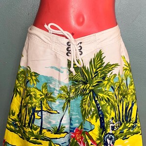 May include: White and patterned swim shorts with a tropical beach scene. The shorts feature a drawstring waist and a colorful design of palm trees, flowers, and a beach landscape. The Hollister logo is visible on the lower right.