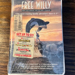 May include: A VHS tape case for the movie Free Willy. The case features a black and white orca whale jumping out of the water. The text on the case reads "Free Willy" and "How far would you go for a friend?" The case also includes a quote from Bab Campbell, "The most rousing family adventure since E.T."