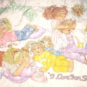 May include: A white and pink quilt with a colorful illustration of six girls having a slumber party. The quilt features the text "I Live For Slumber Parties!"