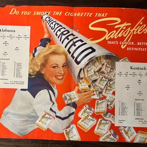 May include: Vintage advertisement for Chesterfield cigarettes. A woman in a cheerleader outfit holds a megaphone filled with cigarette packs. The ad features text: "Do you smoke the cigarette that satisfies?" and team rosters.