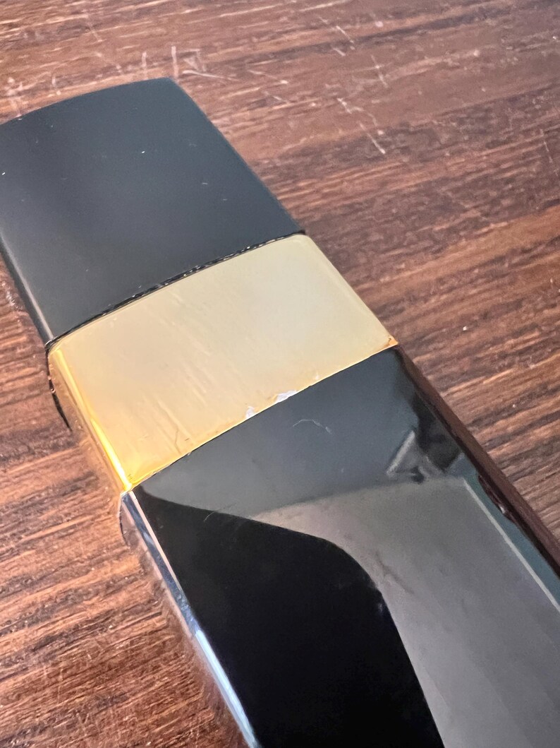 May include: A rectangular object featuring a matte black top section, a central metallic gold band, and a glossy black lower portion. The design is sleek and geometric, with a clear transition between the three distinct color and texture segments.