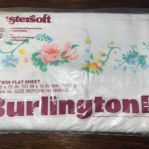 May include: A white twin flat sheet with a floral pattern in pink, blue, and yellow. The sheet is packaged in clear plastic and features the "Burlington" logo in a burgundy color. The sheet is 30 x 75 inches.