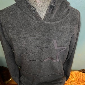 May include: A dark gray fleece hoodie with a large embroidered star and a small pocket on the front. The hoodie has a drawstring hood and a kangaroo pocket.