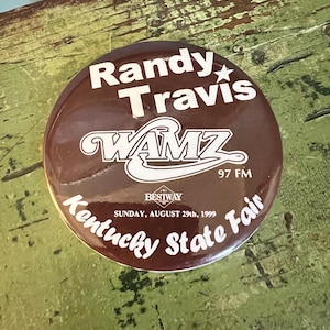 May include: A round, brown button with white text. The button reads "Randy Travis" at the top, with "WAMZ 97 FM" below. The bottom of the button says "Kentucky State Fair, Sunday, August 29th, 1999".