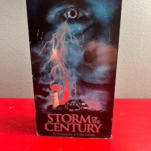 May include: A VHS tape for the movie "Storm of the Century" by Stephen King. The cover features a stormy sky with a lightning bolt and a lighthouse in the distance. The text "An Unspeakable Evil Has Arrived" is printed below the title.