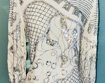 May include: A white long-sleeved shirt with a silver and white geometric pattern. The shirt is covered in sequins and beads.