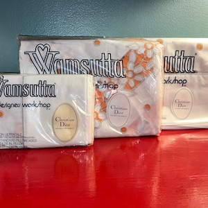 May include: Three white pillowcases with orange floral designs and the text "Wamsutta designers workshop" and "Christian Dior" on the front. The pillowcases are packaged in plastic.