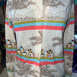 May include: A long-sleeved button-up shirt with a white background and a colorful, abstract print of trees, houses, and waves. The print features shades of brown, blue, green, pink, and red.