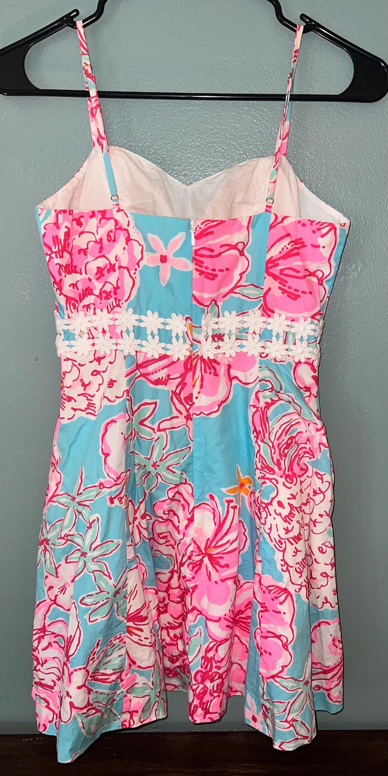 May include: A sleeveless dress featuring a vibrant floral pattern in shades of bright pink, white, and light blue. The dress has a sweetheart neckline, thin spaghetti straps, and a white lace trim detail around the waist with a center back zipper.