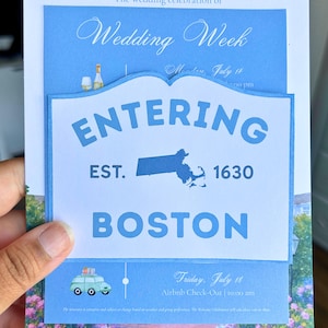May include: Wedding invitation with a light blue and white design. The invitation includes the text "Wedding Week" and "Entering Boston EST. 1630". A small illustration of a car is also present.