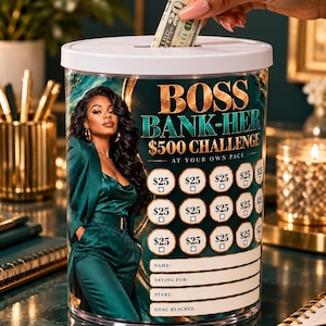 May include: A clear cylindrical money bank with a white lid featuring a graphic of a person in a green suit and the text BOSS BANK-HER $500 CHALLENGE. The surface includes a grid of circles labelled $25 with checkboxes and lines for name, saving for, start, and goal reached.