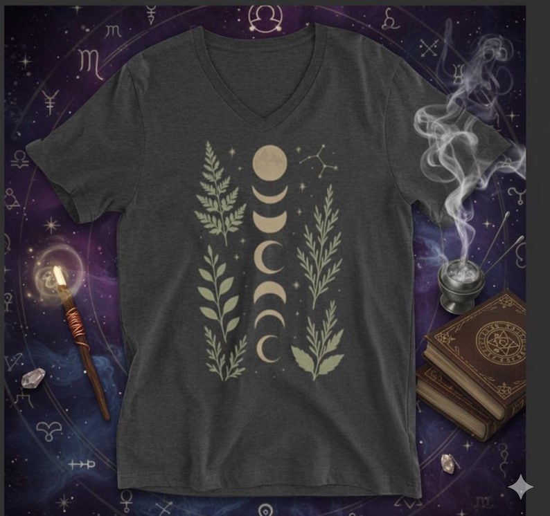 May include: Dark gray V-neck t-shirt featuring a design of moon phases and botanical elements in beige and light green. The shirt has a celestial theme, with a background of astrological symbols.