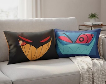 May include: Two decorative throw pillows with cartoon monster faces. One pillow is black with a yellow and orange grin and red eyes. The other is blue with a teal grin and red eyes. The pillows are rectangular.